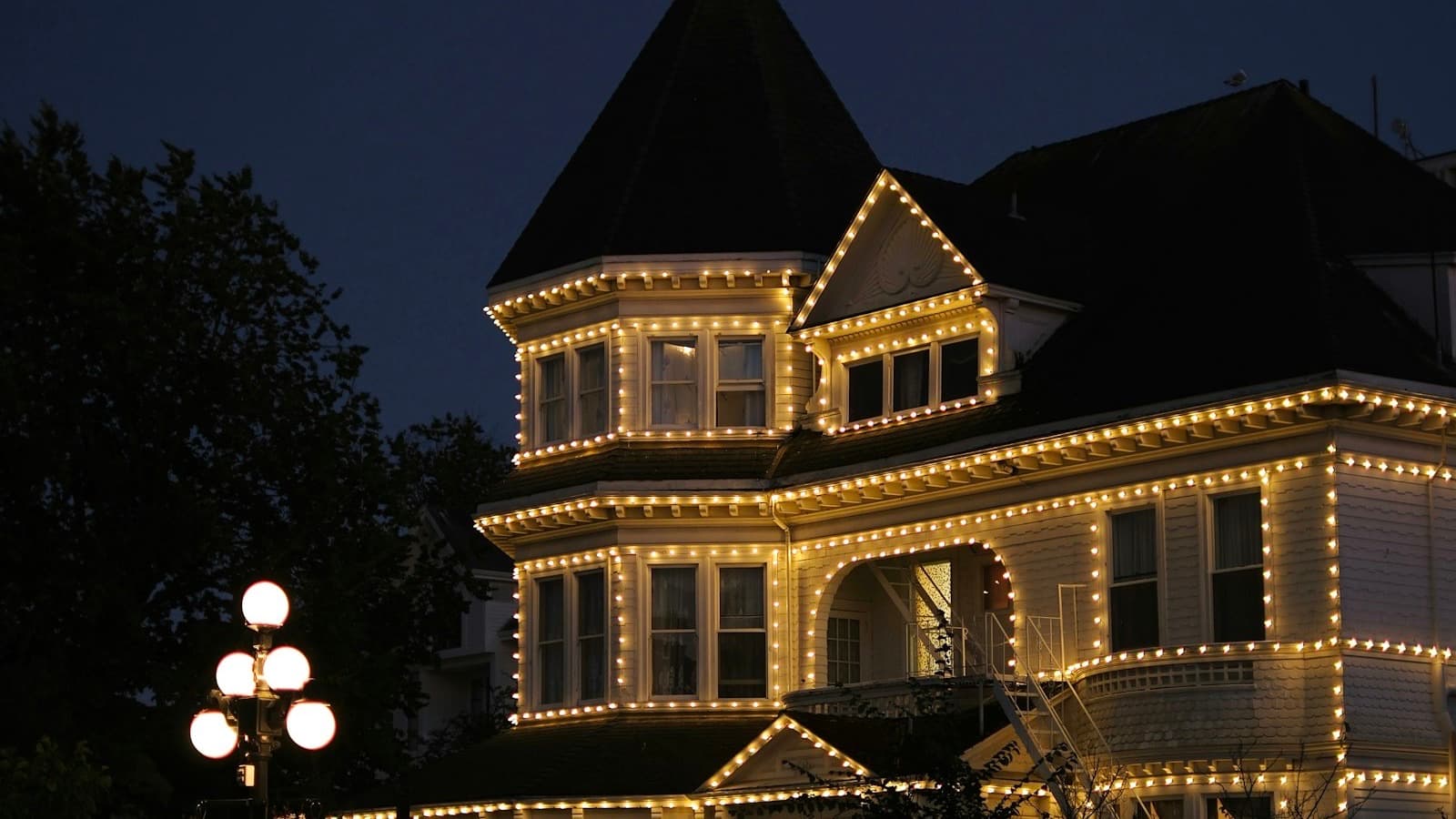 Warm white bulbs outlining the rooflines, gables and bay windows of a house at dusk