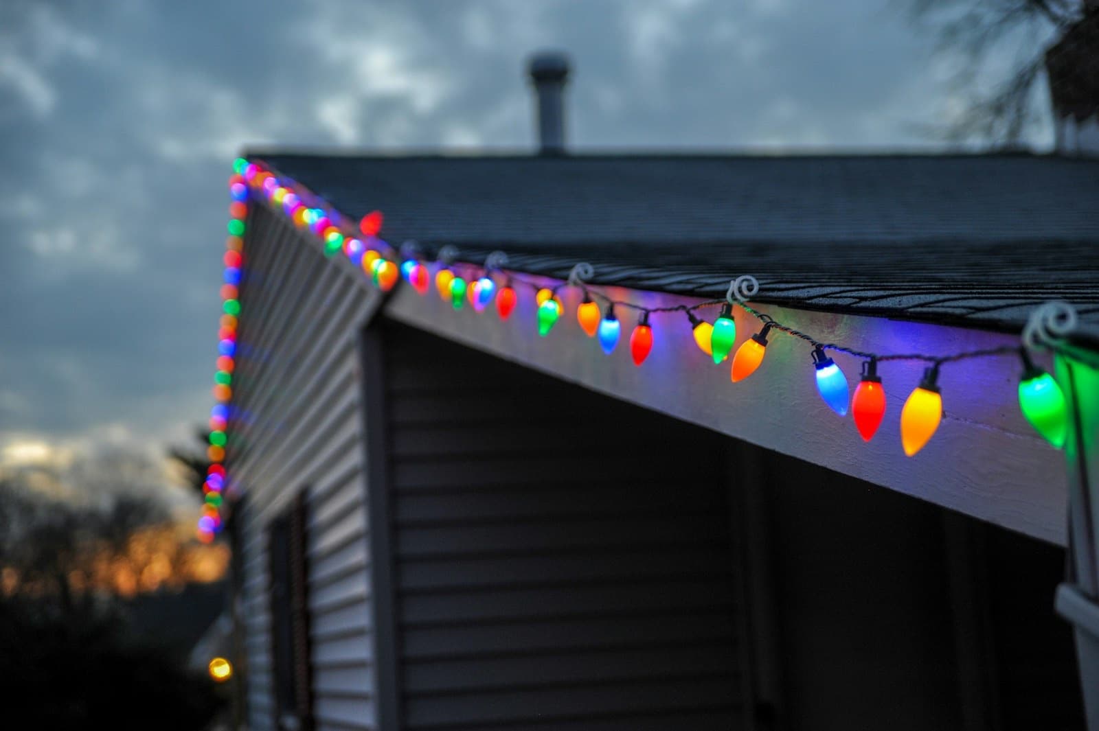 Coloured bulbs clipped along the fascia of a house roofline against a dusk sky